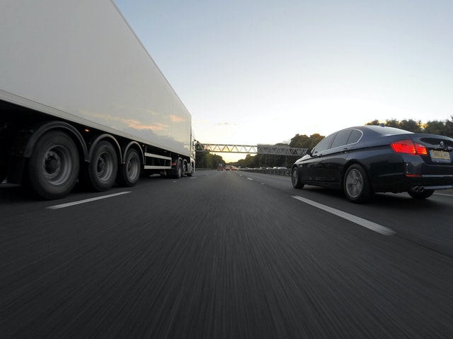 A heavy truck and a medium size sedan traveling on a highway