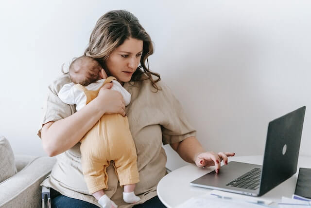 Mother holding a baby while working on her laptop
